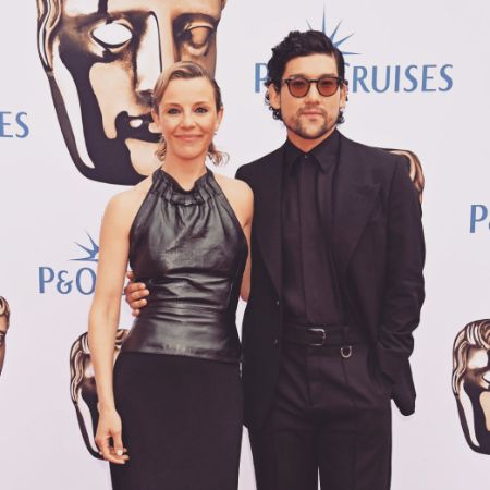 Sophia Di Martino and Will Sharpe are standing in the red carpet in all black clothes.